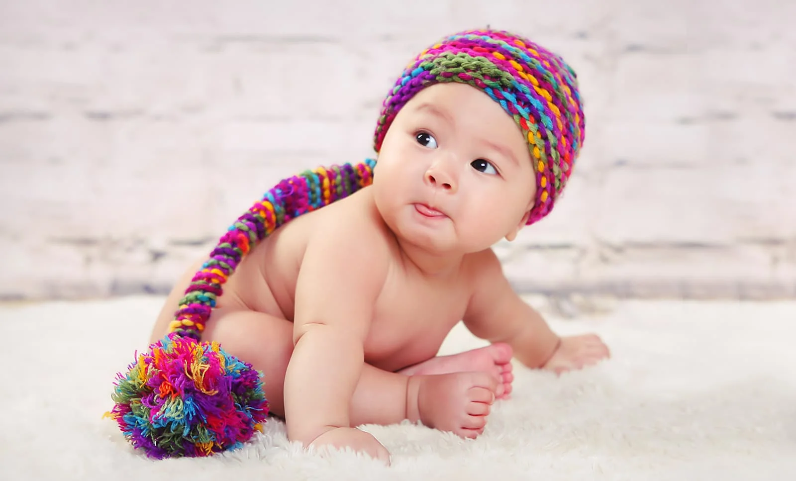 Hình ảnh em bé tập bò đội mũ len nhiều màu sắc đuôi dài trên nền trắng