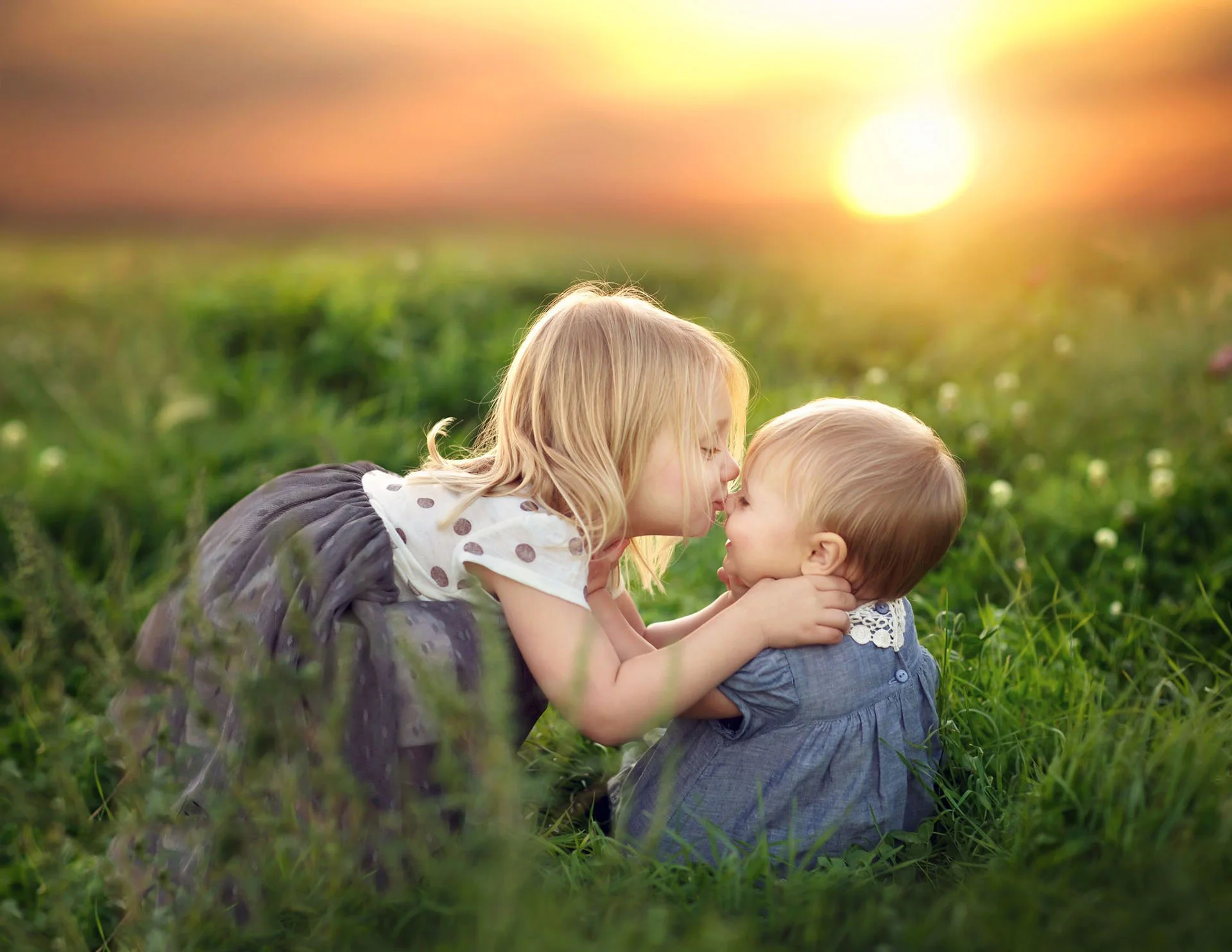 Hai anh chị em bé chơi đùa trên cánh đồng cỏ lúc hoàng hôn