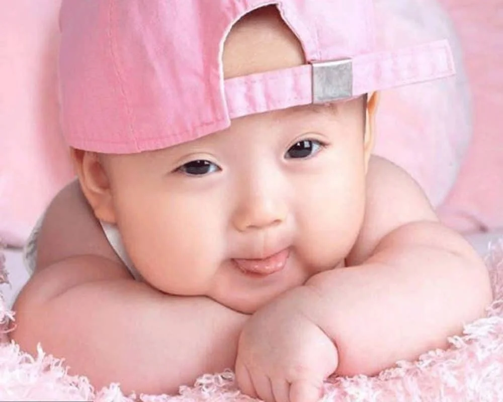 Hình ảnh em bé sơ sinh đội mũ lưỡi trai màu hồng nằm trên chăn nhung dễ thương