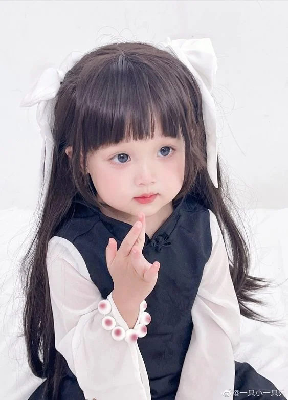 Bé gái tóc dài đeo nơ trắng mặc váy đen thanh lịch