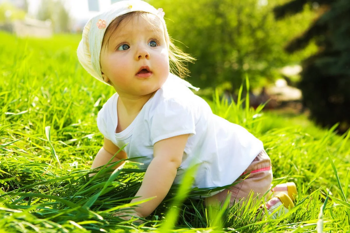 Em bé tập bò trên bãi cỏ xanh mướt ngoài trời