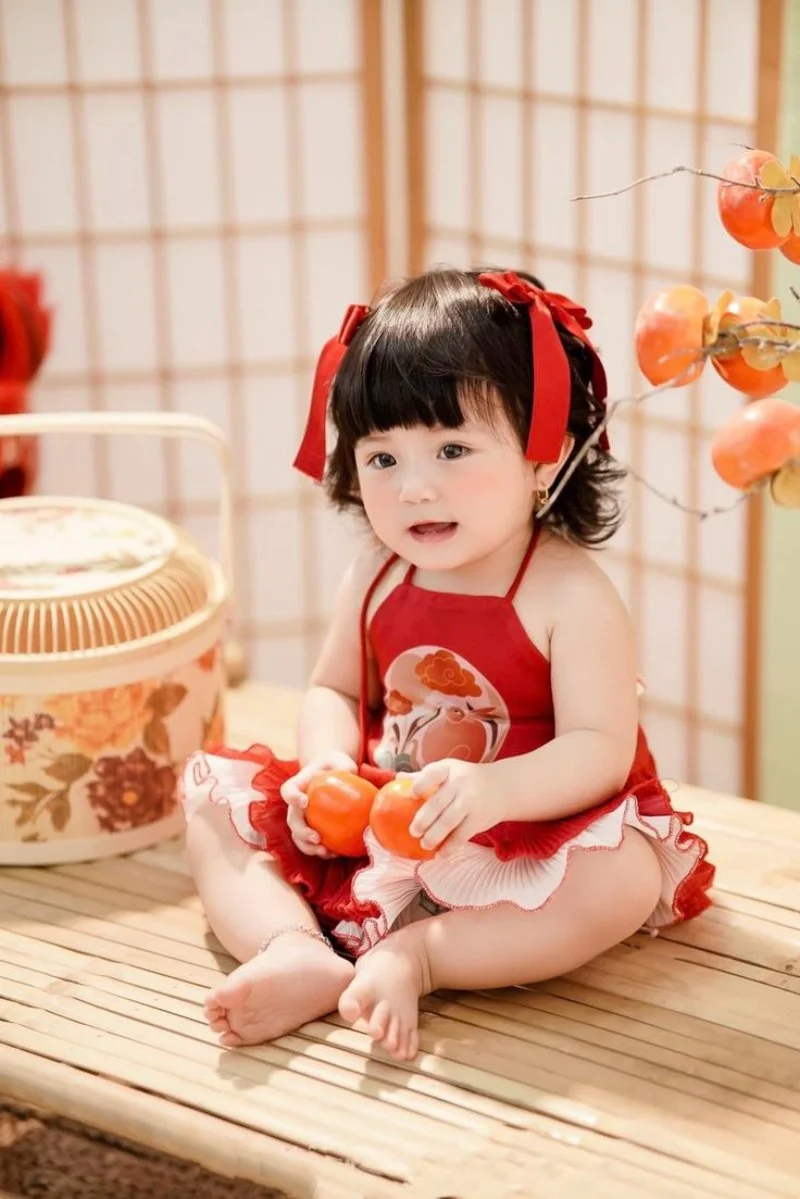 bé gái mặc váy đỏ ngồi trên chiếu