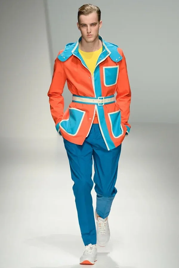 Nam model đi trên runway với bộ đồ màu cam và xanh, ví dụ điển hình về bảng màu phối đồ.