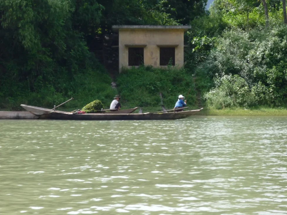 Phong cảnh thiên nhiên yên bình với người dân chèo thuyền trên sông và ngôi nhà nhỏ bên bờ.